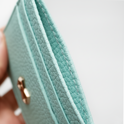 Gros plan sur la texture grainée d’un porte-cartes de crédit en cuir taurillon de couleur menthe, révélant la finesse du cuir et la précision des coutures.