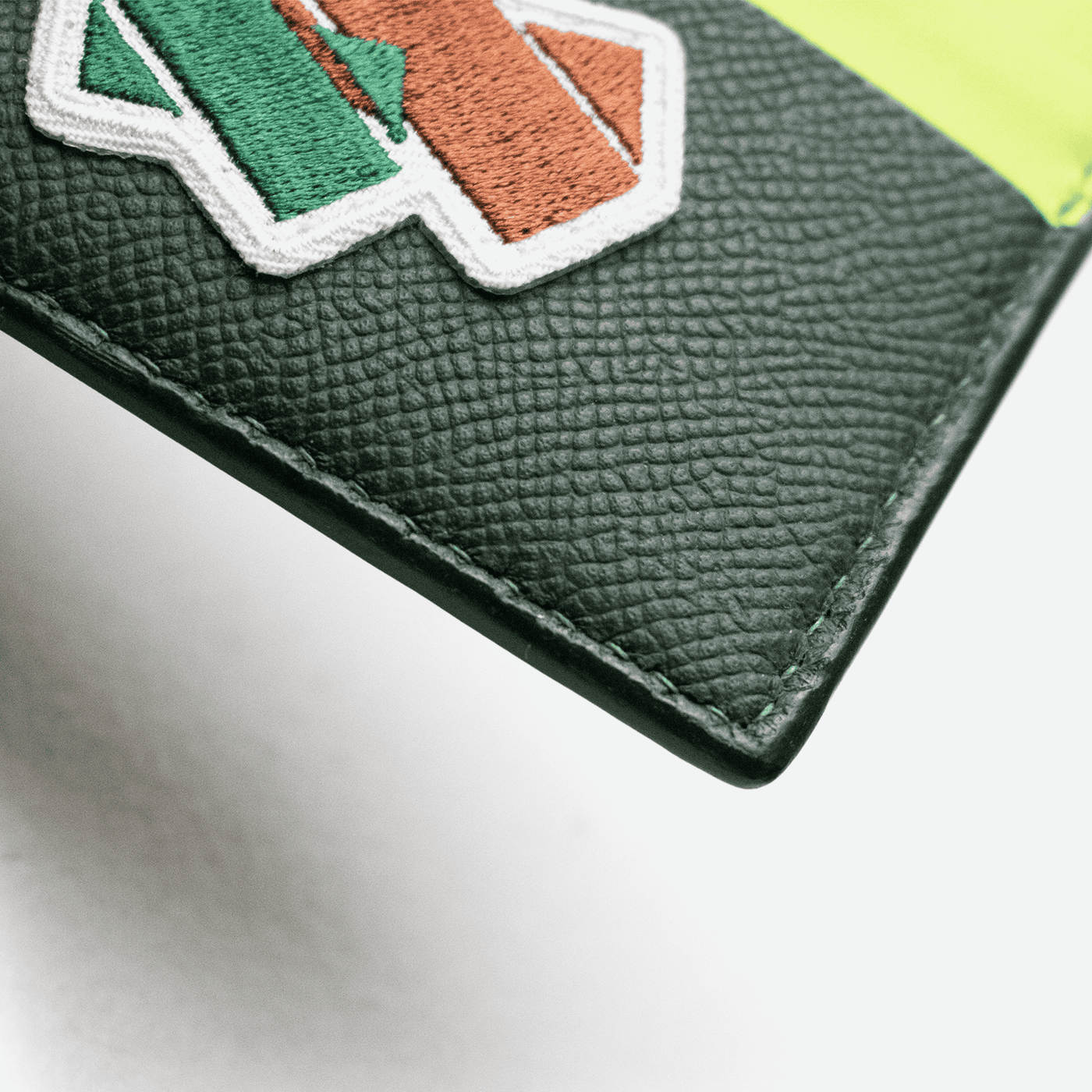 Zoom des détails du porte-cartes en cuir grainé vert et fil de lin vert.