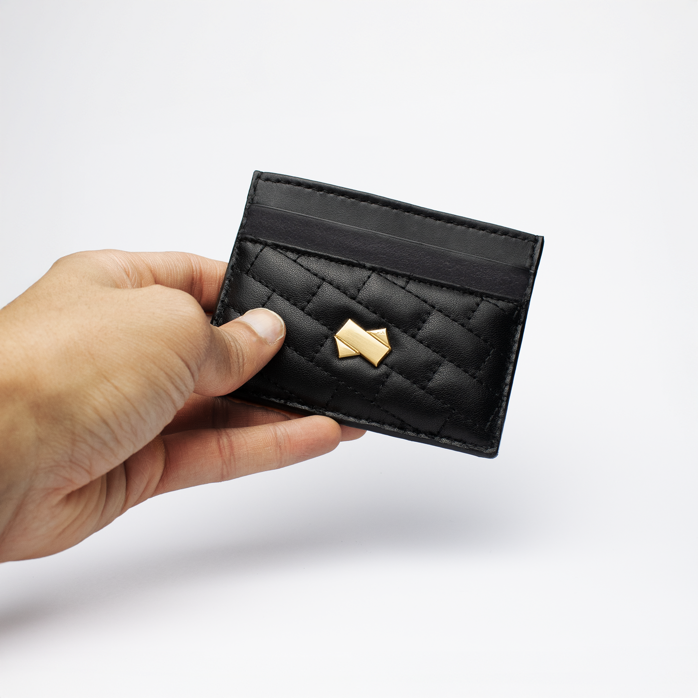 Main tenant un porte cartes cuir noir matelassé avec signature Faubret doré, vue pratique