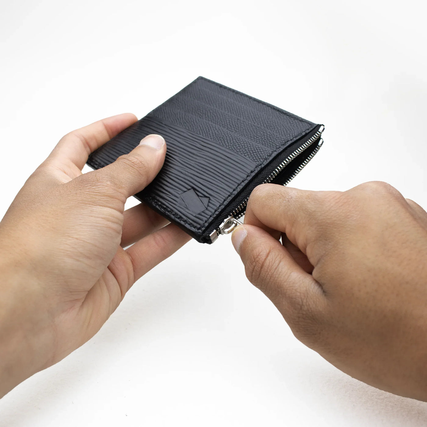 Main ouvrant le porte-cartes Faubret noir grâce à sa fermeture éclair argentée.