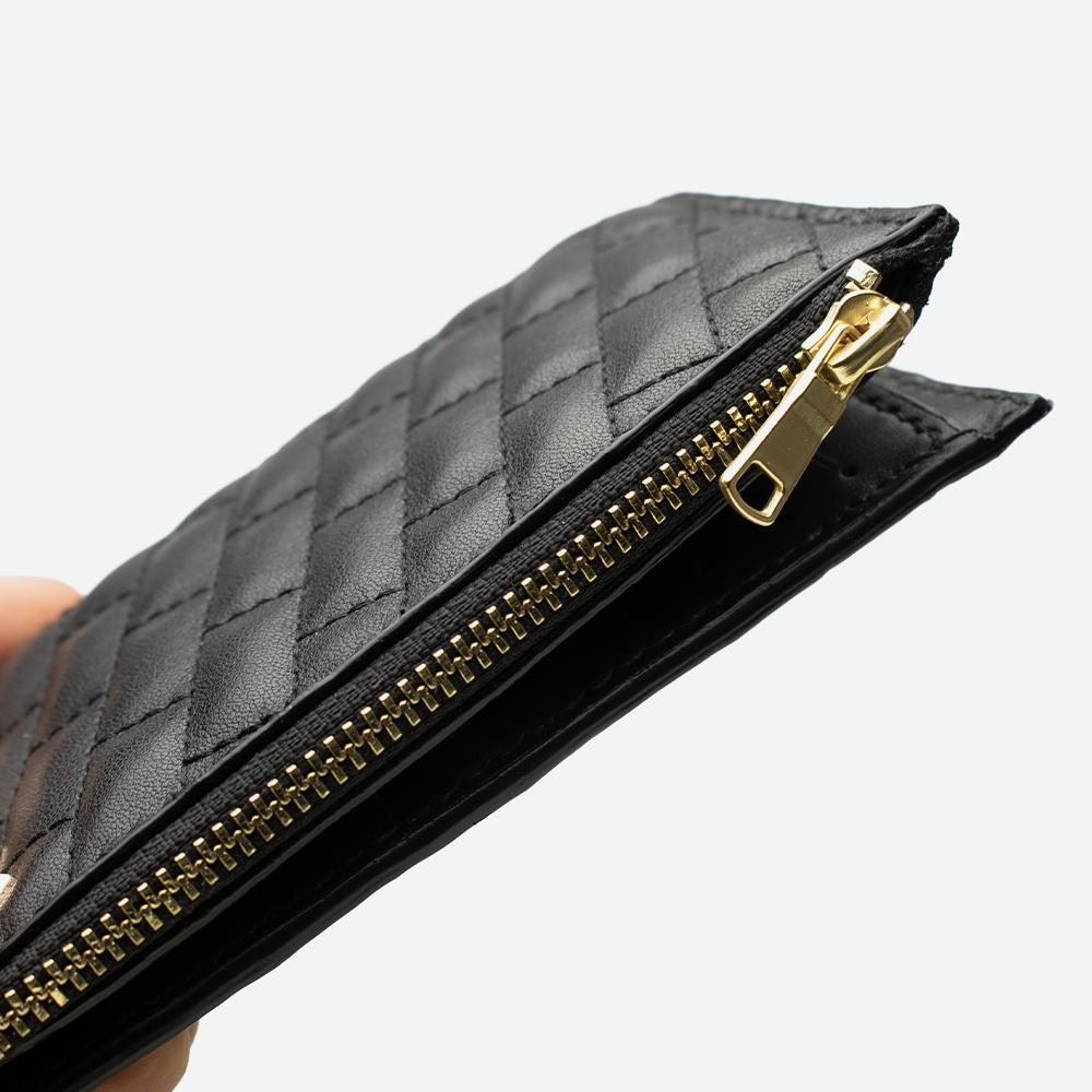 Détail de la fermeture éclair dorée du porte-carte femme FAUBRET sur cuir noir.