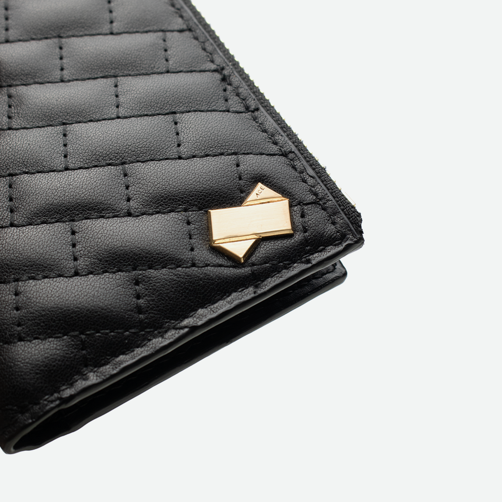 Gros plan sur le logo métallique doré FAUBRET fixé sur le cuir noir matelassé du porte-carte.